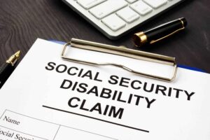 A social security disability claim application on a clipboard sitting on a desk near a computer keyboard.