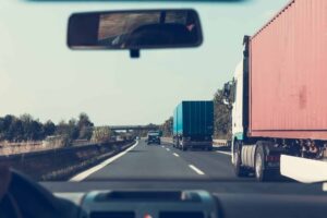 An inside POV of what the driver of a car sees on the highway with two tractor trailers beside the vehicle.